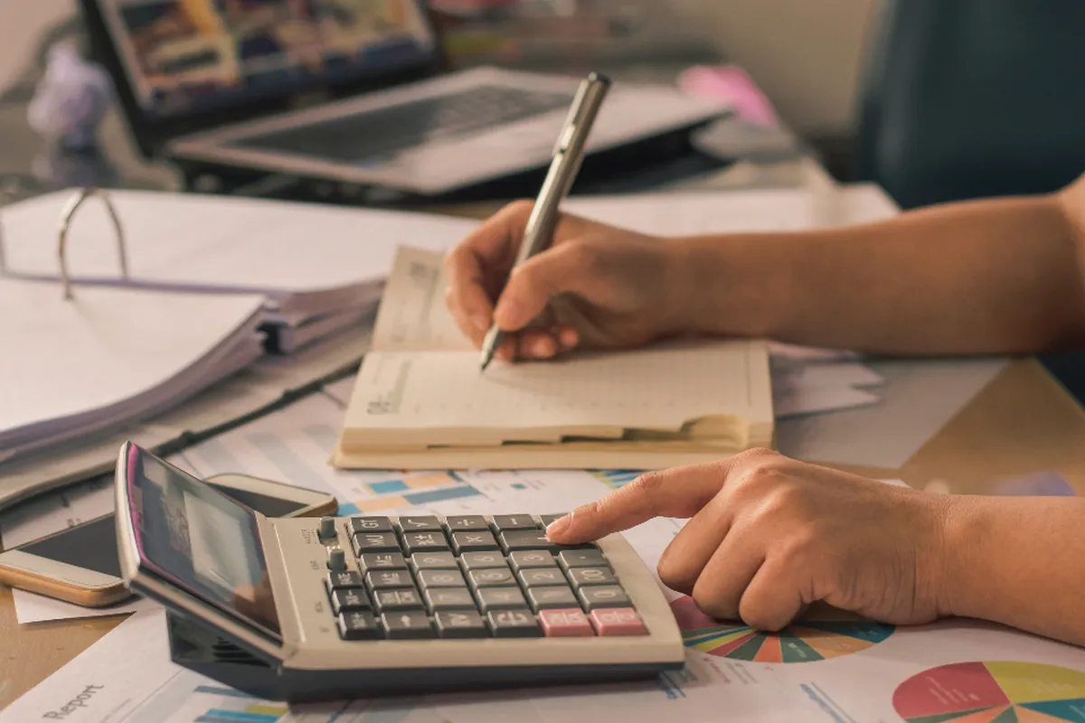 Hands using a calculator and writing in a notebook while working through a care budget